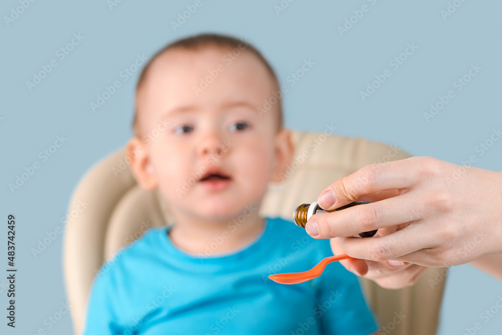 Mom pours the syrup with the medicine into a spoon, the toddler looks curiously at the spoon with vitamins. Mom pours the syrup with the medicine into a spoon, the toddler looks curiously at the spoon with vitamins.