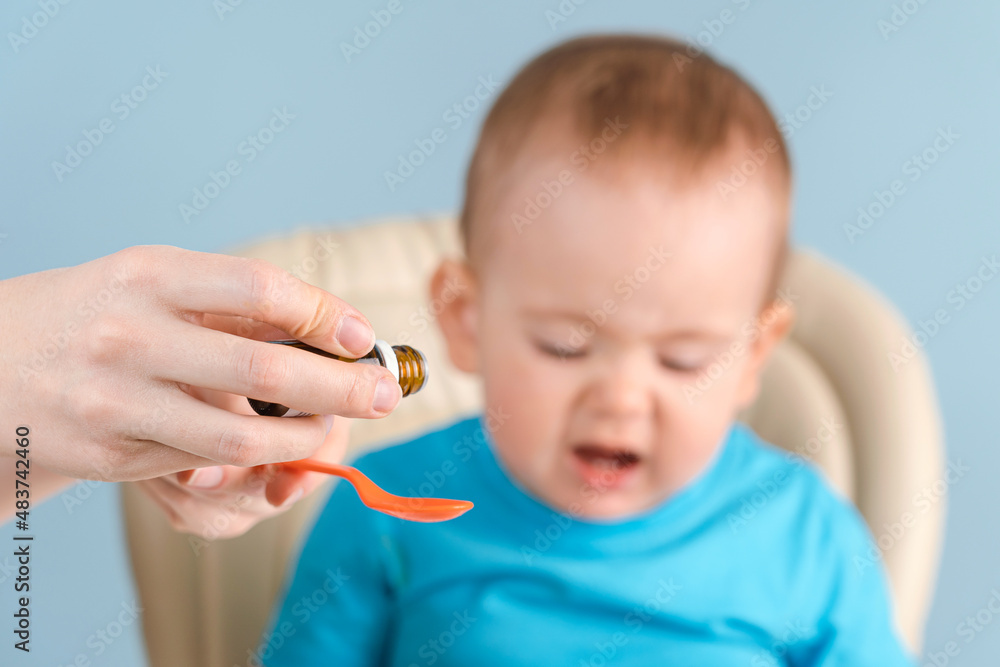 Mom pours syrup with medicine into a spoon, toddler cries and refuses to drink medicine. Mom pours syrup with medicine into a spoon, toddler cries and refuses to drink medicine.