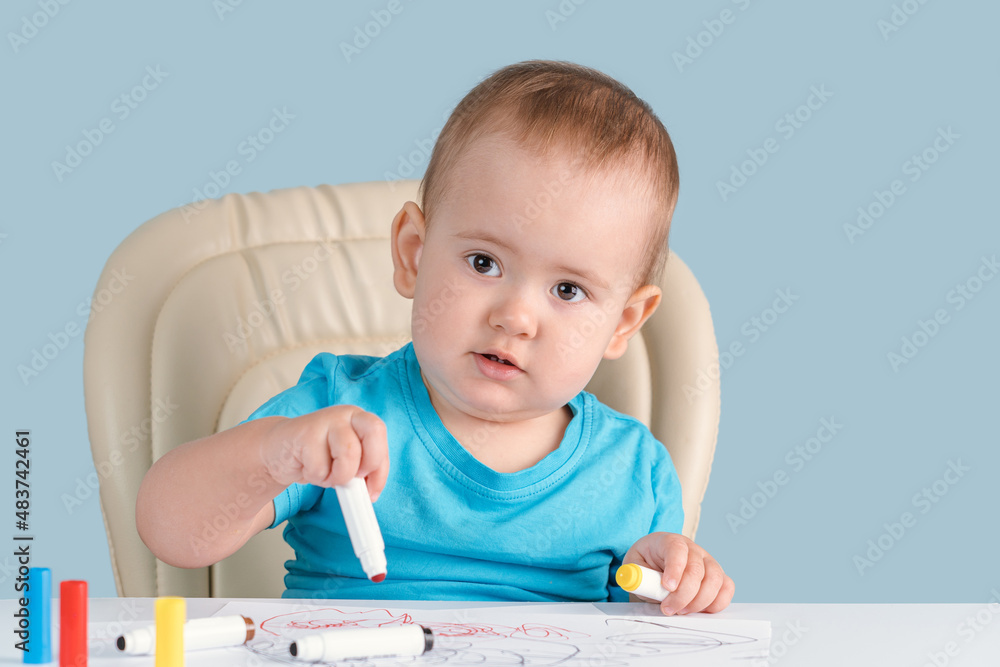 A baby of 12-17 months draws with felt-tip pens sitting on a child's chair A baby of 12-17 months draws with felt-tip pens sitting on a child's chair