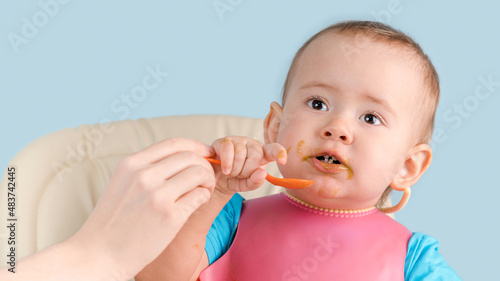 Mom teaches a newborn baby 12-17 months old to use a spoon while eating