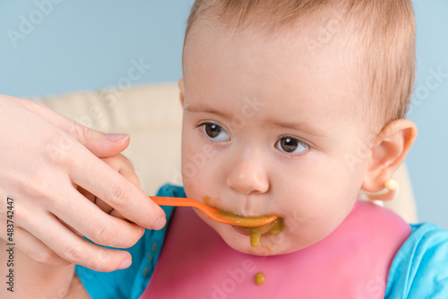 Mom feeds baby 12-17 months with a spoon of green vegetable puree