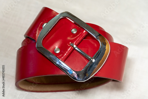 Red belt made of thick genuine leather on a white background made of linen fabric. Production of handmade belts from natural environmentally friendly materials.