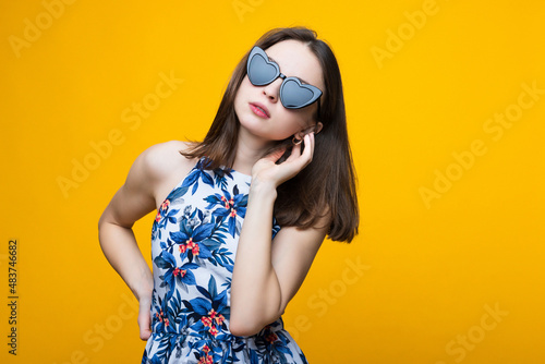 Portrait of a beautiful young woman in a dress and sunglasses on a yellow background
