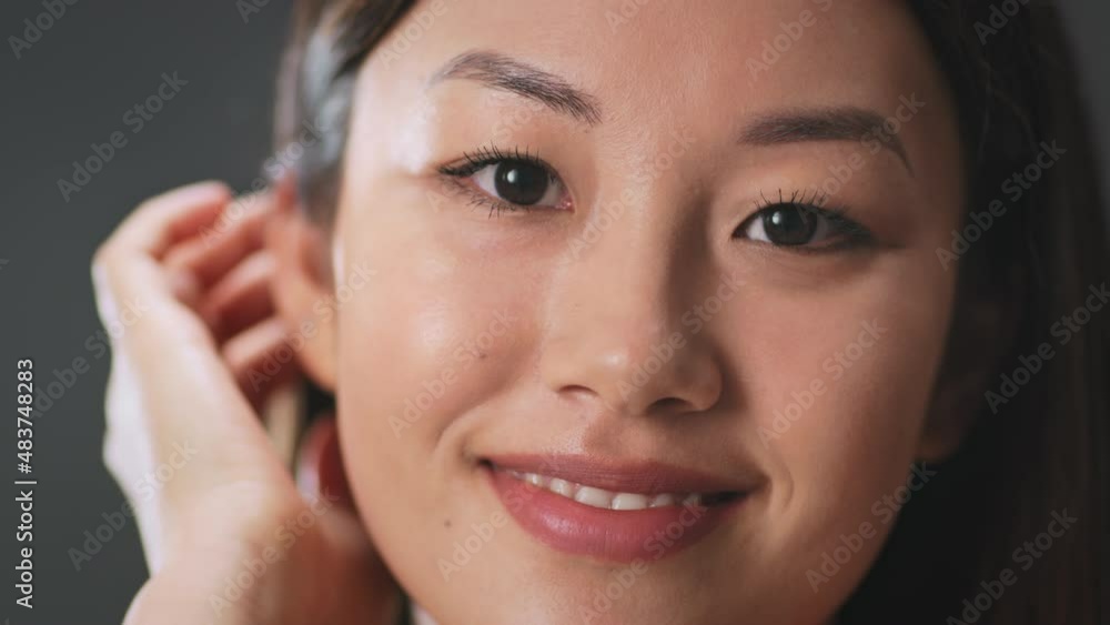 Beauty and wellness concept. Young well groomed shy asian woman flirting to camera, fixing her hair and smiling, closeup Beauty and wellness concept. Young well groomed shy asian woman flirting to camera, fixing her hair and smiling, closeup
