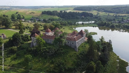 Aerial drone shot of historic castle on hill near lake, medieval architecture and cultural landmark in rural Svirzh, near Lviv Ukraine on warm sunny summer day. Tourist and travel attraction.