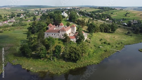 Aerial drone shot of historic castle on hill near lake, medieval architecture and cultural landmark in rural Svirzh, near Lviv Ukraine on warm sunny summer day. Tourist and travel attraction.