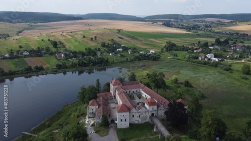 Aerial drone shot of historic castle on hill near lake, medieval architecture and cultural landmark in rural Svirzh, near Lviv Ukraine on warm sunny summer day. Tourist and travel attraction.