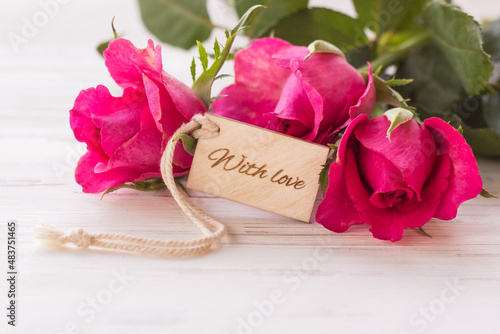 Roses and tag with the text With love on a white wooden background. Close-up. greeting card