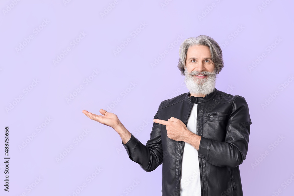 Senior man in leather jacket pointing at something on lilac background Senior man in leather jacket pointing at something on lilac background