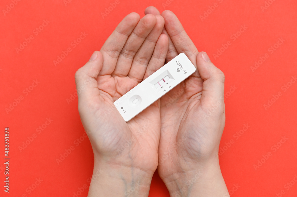 A positive rapid test for covid-19 in the hands of a teenager on a red background. A positive rapid test for covid-19 in the hands of a teenager on a red background.
