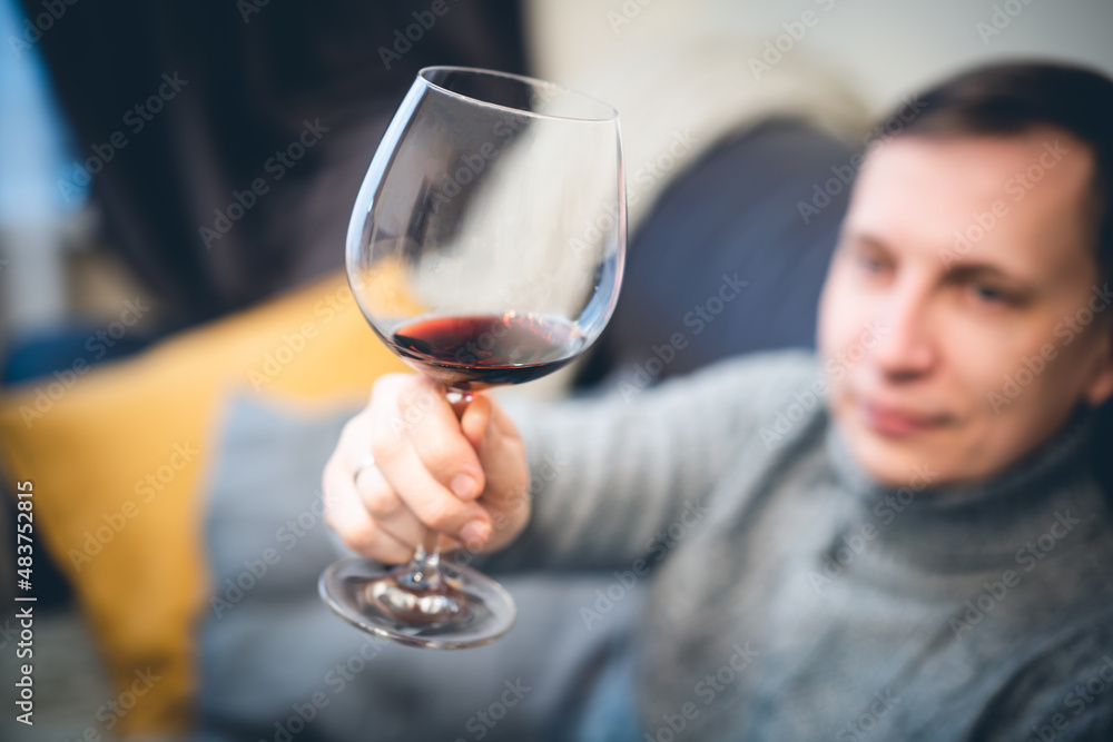 Relaxed serene rich lonely middle aged single man drinking red wine relaxing on sofa at home, enjoying resting sitting on couch holding glass tasting and reflecting.