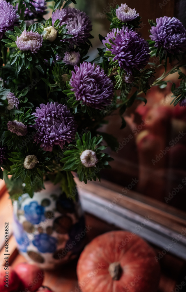A bouquet of lilac asters, a pumpkin, and garden apples on a wooden windowsill