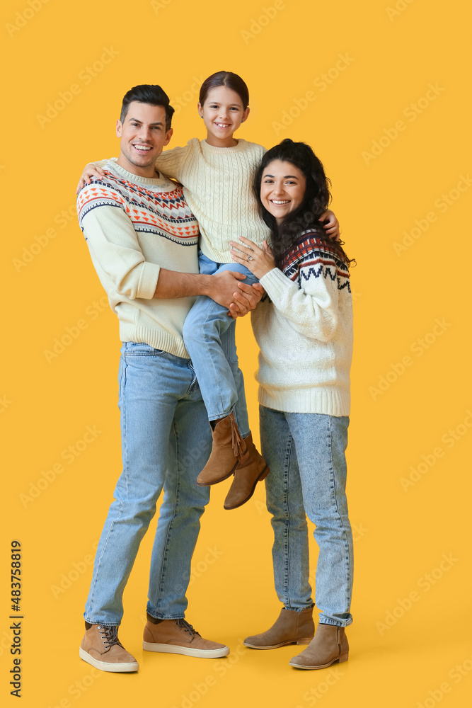 Happy parents with little daughter in warm sweaters on yellow background Happy parents with little daughter in warm sweaters on yellow background