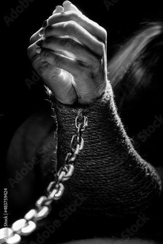 Women's hands are tied with a rope and shackled with a metal chain