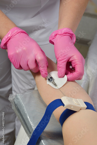 A nurse in pink sterile gloves gives an injection into the arm intravenously. A doctor in a white coat bandaged his hand with a tourniquet and gives an injection into a vein. The doctor vaccinates
