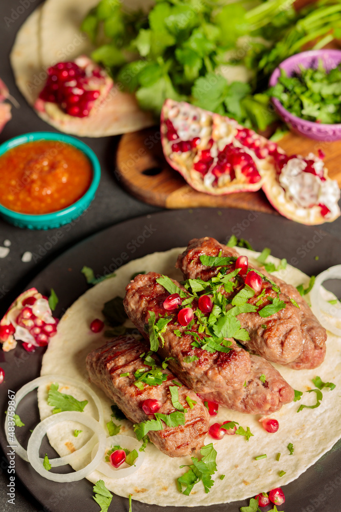 Kebabs on the pit, with coriander greens, onions and pomegranate seeds. Close-up, ingredients in the background. Vertical