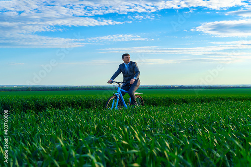 business concept - A businessman rides a bicycle on a green grass field, dressed in a business suit, he has a briefcase and documents