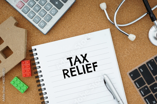 TAX RELIEF wording on a note book over brown surface with a few item related with medical, education, property and financial