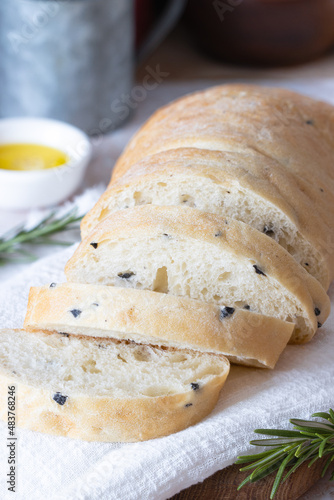 sliced wheat ciabatta with olives on a white towel. Wheat homemade bread, olive oil and rosemary