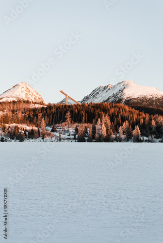 Landscape photo of frozen and snow covered Strba tarn (Strbske pleso) in winter time. Mountains in Slovakia with frozen lake on foreground in early morning sunrise.