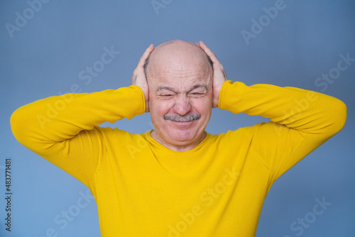 Fotografie Senior man covering his ears with raised palms having terrible headache