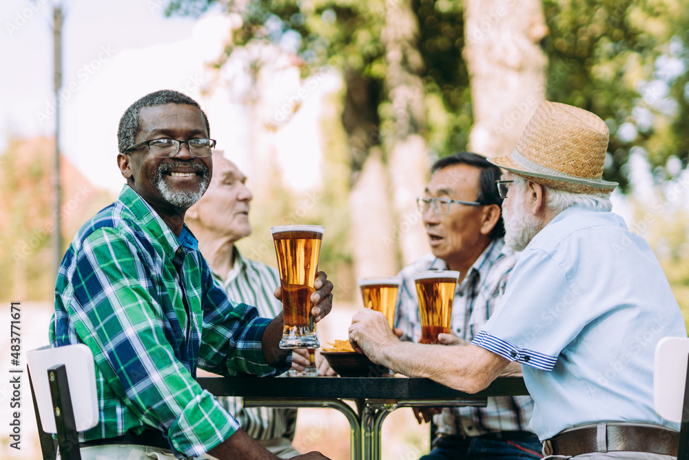 Group of senior friends drinking a beer at the park. Old multiethnic friends making activities outdoor. Concept about third age and lifestyle