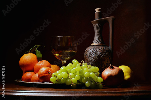 martwa natura z owocami na brązowym tle. winogron, granat, pomarańcz, czerwone róże w kompozycji z butelka wina. kompozycja na tekstura lub tapeta na pulpit. 