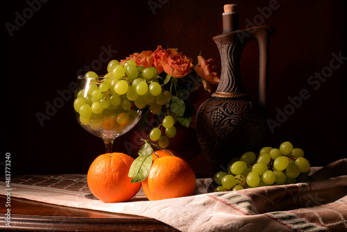 martwa natura z owocami na brązowym tle. winogron, pomarańcz, czerwone róże w kompozycji z butelka wina. kompozycja na tekstura lub tapeta na pulpit. 