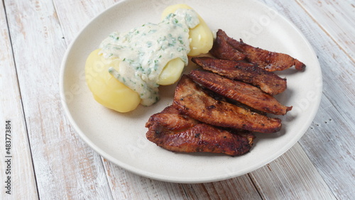 Crispy fried pork with creamy parsley sauce and boiled potato in the plate on the table or stegt flæsk, a classic Danish cuisine. photo