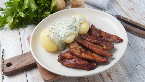 Crispy fried pork with creamy parsley sauce and boiled potato in the plate on the table or stegt flæsk, a classic Danish cuisine.
