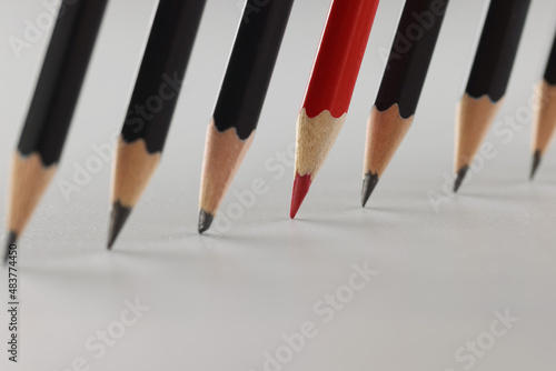 Red sharp pencil among black pencils in a row
