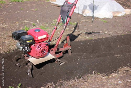 a red walk-behind tractor stands on plowed land, preparing a garden for planting plants and seedlings in spring