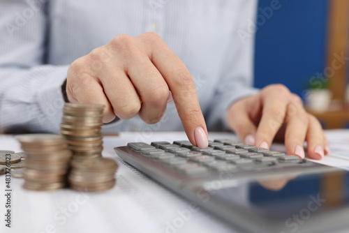 A woman counts on a gray calculator near the coins,