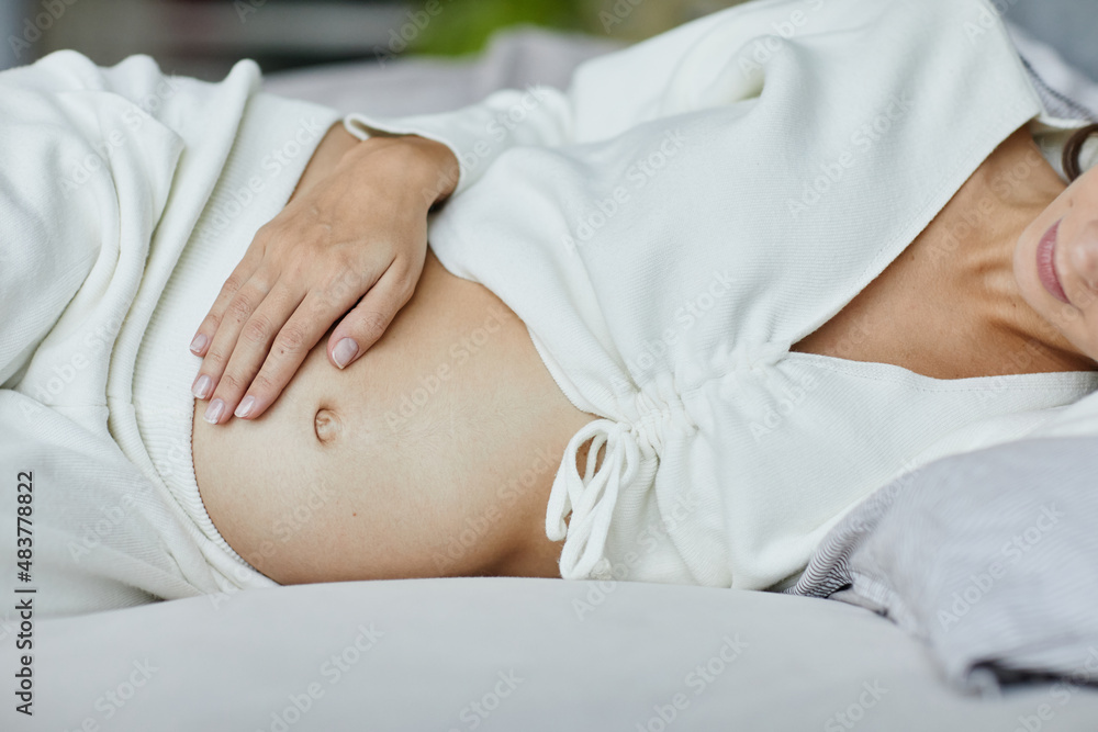 Close-up of young pregnant woman touching her belly lying on her bed in bedroom Close-up of young pregnant woman touching her belly lying on her bed in bedroom