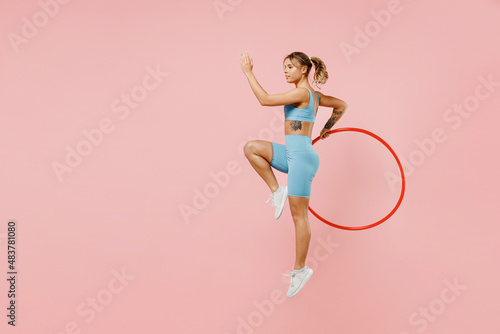 Full size young strong sporty athletic fitness trainer instructor woman wear blue tracksuit spend time in home gym hold hula hoop isolated on pastel plain light pink background. Workout sport concept.