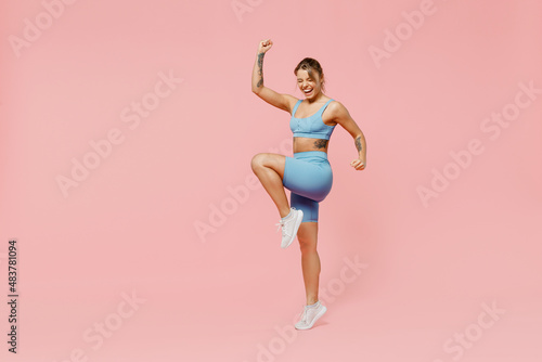 Full body young strong sporty athletic fitness trainer instructor woman wear blue tracksuit spend time in home gym do winner gesture isolated on pastel plain pink background. Workout sport concept
