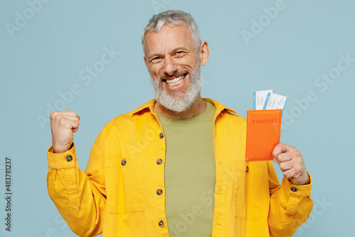 Traveler tourist elderly gray-haired bearded man in shirt hold passport ticket do winner gesture isolated on plain blue background Passenger travel abroad weekends getaway. Air flight journey concept
