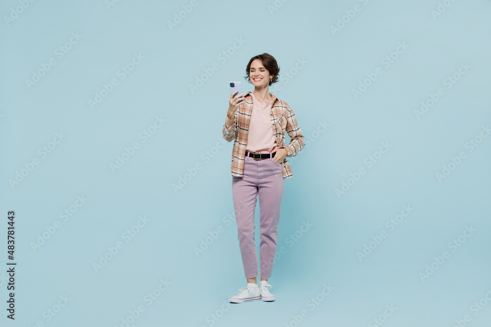 Full body young smiling happy woman 20s wearing casual brown shirt hold in hand use mobile cell phone isolated on pastel plain light blue color background studio portrait. People lifestyle concept Full body young smiling happy woman 20s wearing casual brown shirt hold in hand use mobile cell phone isolated on pastel plain light blue color background studio portrait. People lifestyle concept