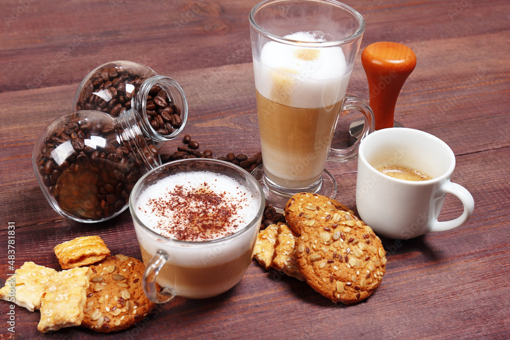 Cups of espresso, latte and cappuccino, crackers, cookies, holder with ground coffee, tamper and coffee beans on wooden table. Cups of espresso, latte and cappuccino, crackers, cookies, holder with ground coffee, tamper and coffee beans on wooden table.
