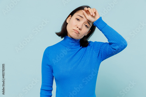 Young woman of Asian ethnicity 20s years old wear blue shirt woman put hands on head rub temples having headache suffering from migraine isolated on plain pastel light blue background studio portrait