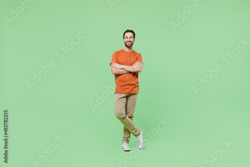 Full body young smiling fun man 20s wear casual orange t-shirt isolated on plain hold hands crossed folded look camera pastel light green color background studio portrait. People lifestyle concept.