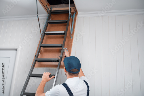 a uniformed specialist fixes a metal ladder to the hatch of the attic door.