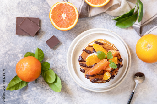 Celebrating Pancake day, healthy breakfast. Delicious homemade american bananas pancakes with chocolate and red orange on grey stone background. Flat lay, top view.