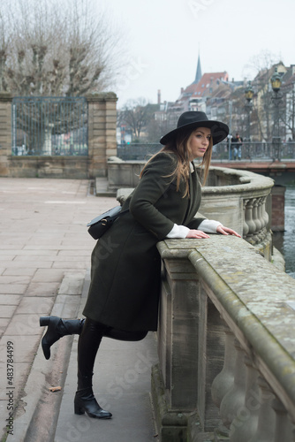 Portrait of young woman wearing a winter green coat, leather boots and hat in the street