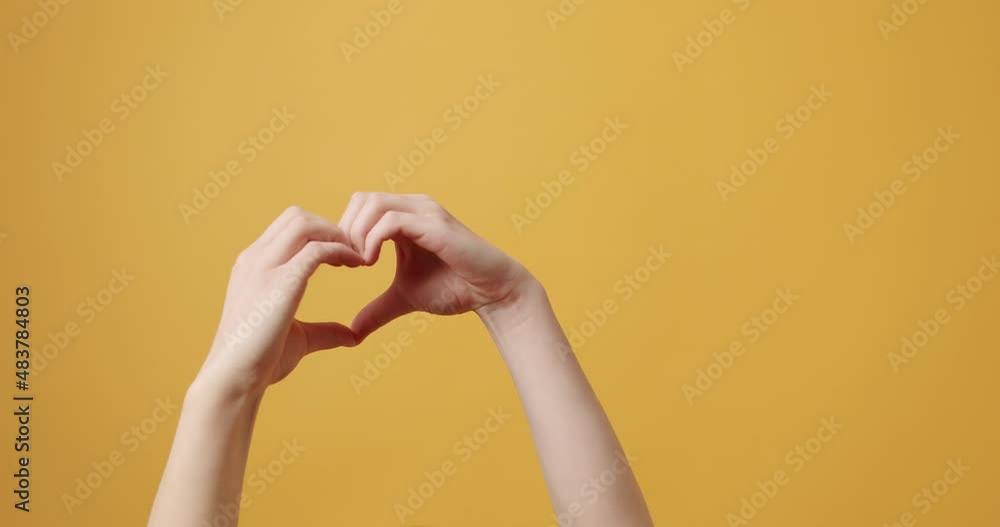 Young beautiful girl makes heart by her hands in heart shape on isolated yellow background for Banner and Text message. Hands in shape of love heart, Love concept. connect hands to make heart shape Young beautiful girl makes heart by her hands in heart shape on isolated yellow background for Banner and Text message. Hands in shape of love heart, Love concept. connect hands to make heart shape