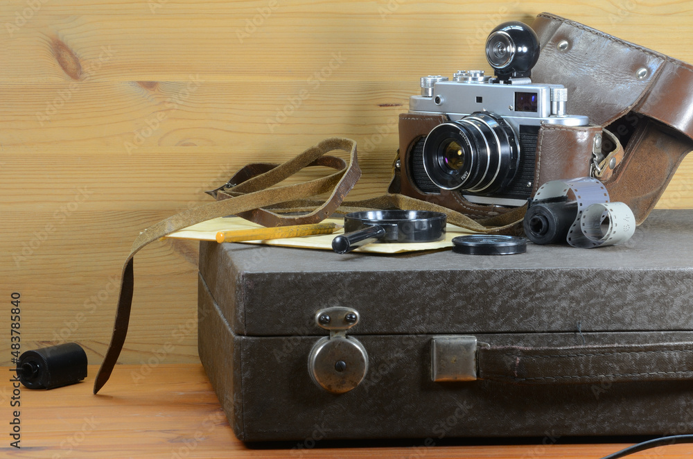 An old film camera lies on a suitcase with a photographic enlarger, on a wooden background.