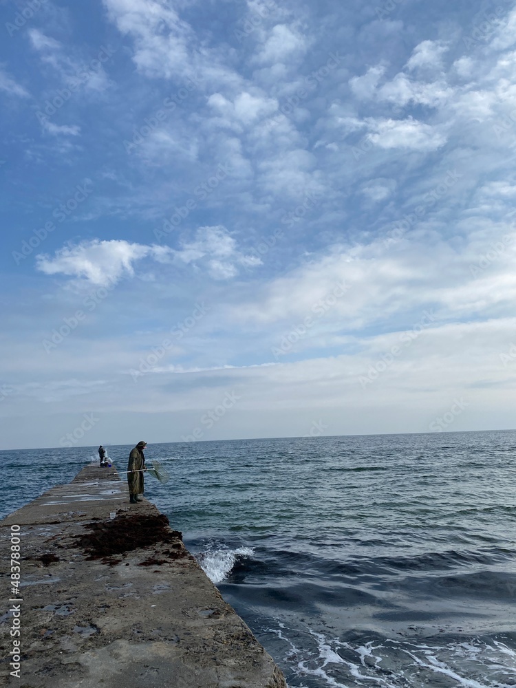 Vertical shot of unrecognizable fisherman standing on a pier, fishing in the sea