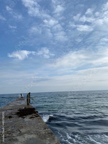 Vertical shot of unrecognizable fisherman standing on a pier, fishing in the sea © Ihor
