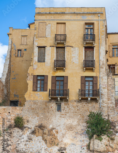 Chania, Crete, Greece - October 2, 
 2021 Old yellow stone building with windows at the old Venetian port in Chania, Crete. Sunny summer day with blue sky