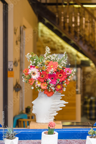 Colorful bouquet decorative gerber flowers in a white ceramic vase in the shape of a head, standing on the windowsill